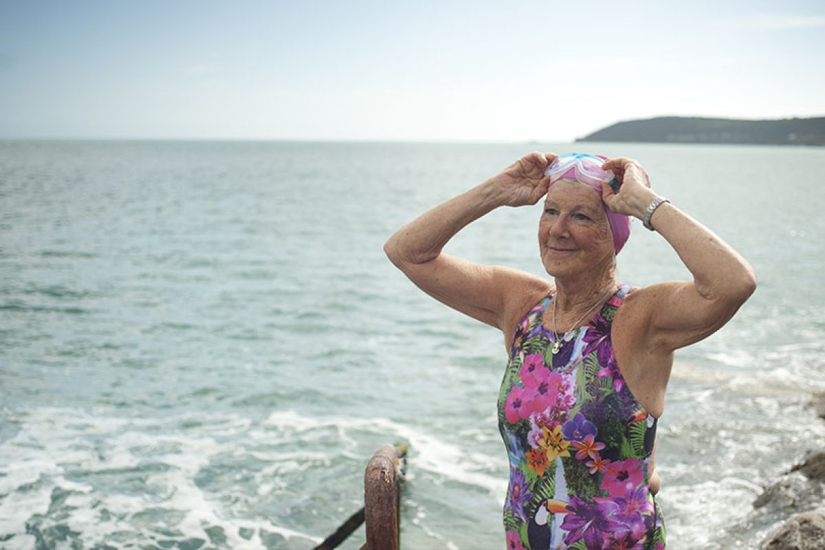 an older lady in a colorful swimsuit prepares for a swim in the ocean
