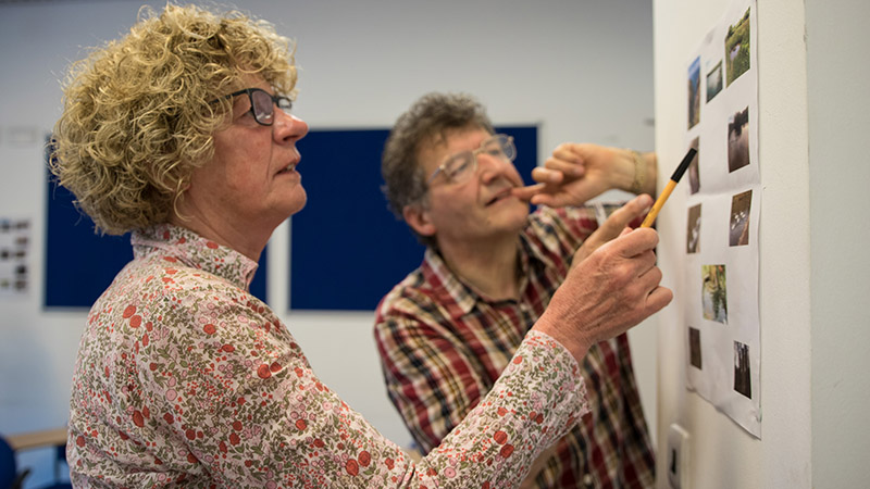 Two HEPE members discuss images stuck to a wall