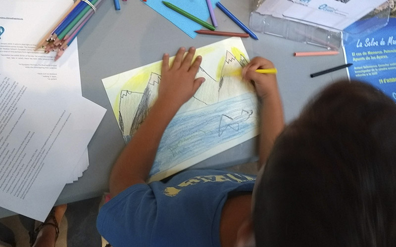 A child draws a scene of mountains and sea
