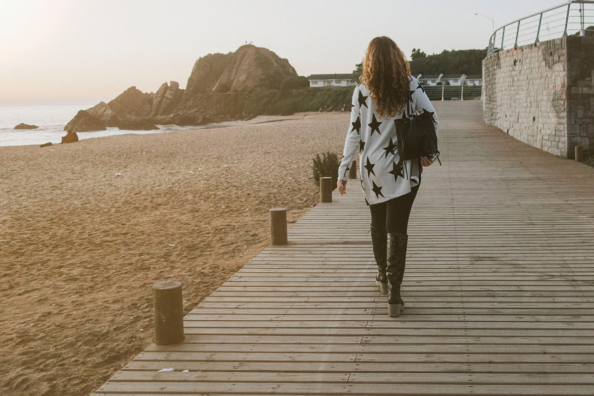 A woman walks along a boardwalk next to the beach