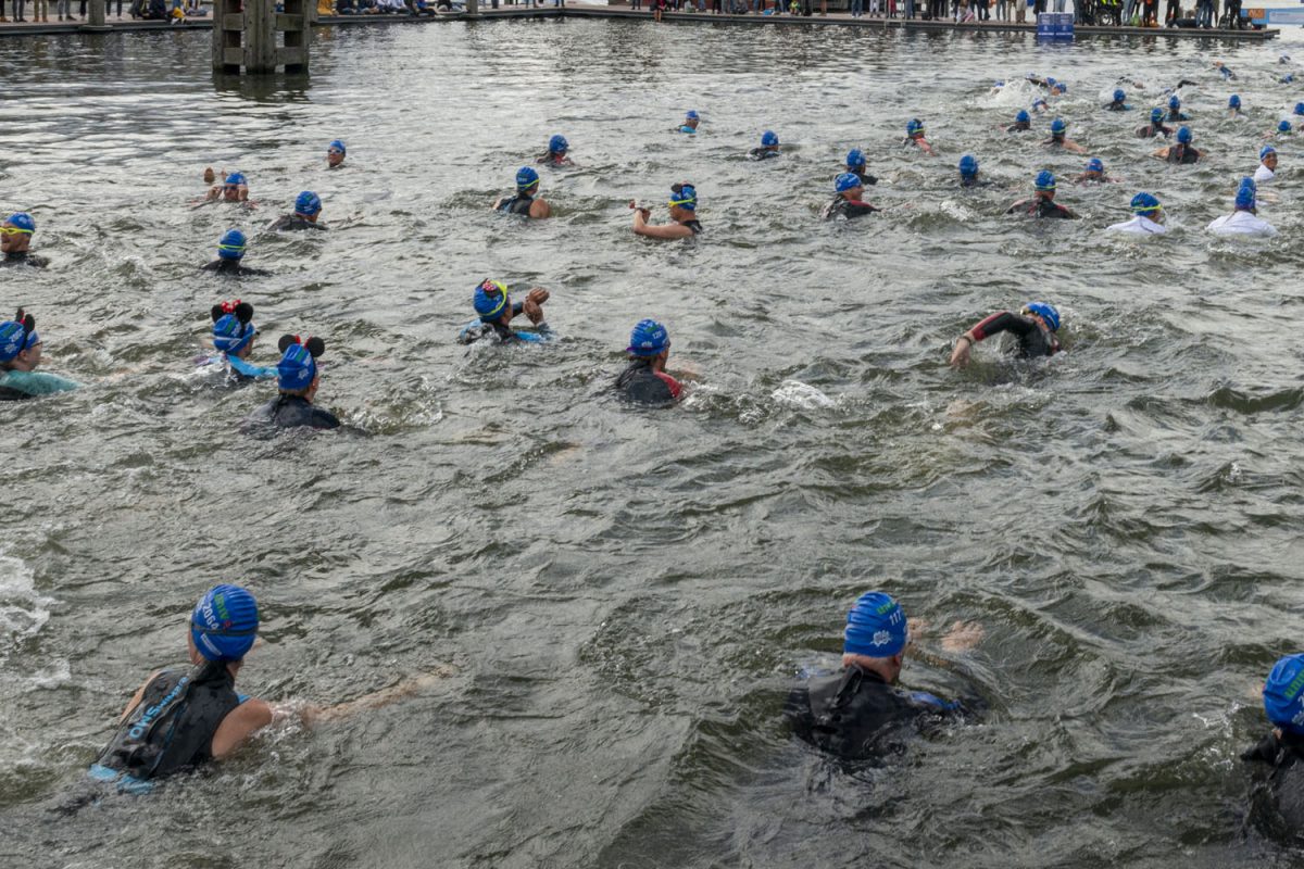 People with blue hats swim in the waters of Amsterdam